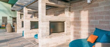 An outdoor patio with a stone wall, a pergola, and a seating area with cushions.