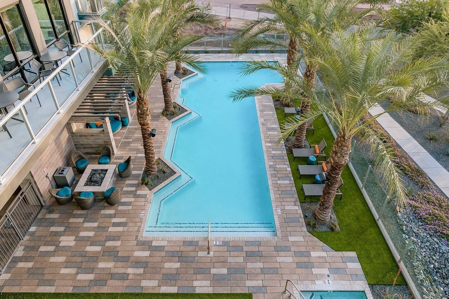 A rooftop pool with palm trees, lounge chairs, and a glass balustrade.