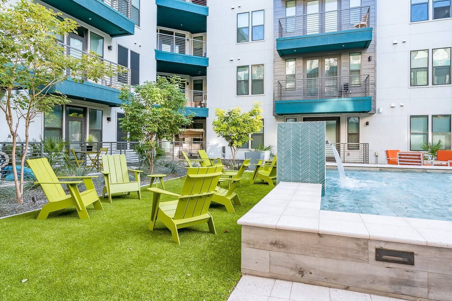 A modern building with a rooftop pool, green lawn, and outdoor seating area with chairs.