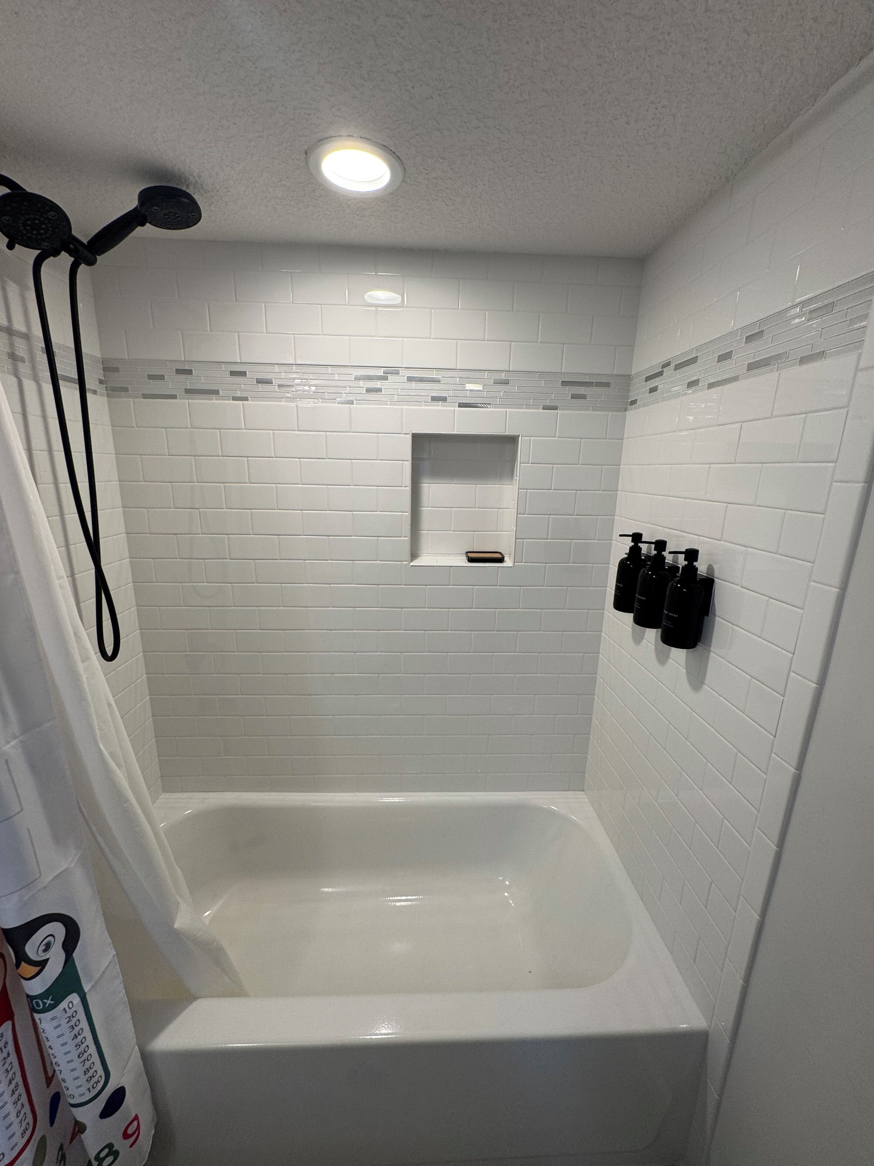 Ein Badezimmer mit einer weißen Badewanne, einer Duschbrause und einem Ablagefach für Toilettenartikel.