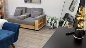 Un salon moderne avec un canapé gris, un fauteuil bleu, une table basse noire, un grand miroir et un tableau représentant un paysage urbain accroché au mur.