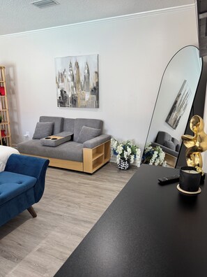 Ein modernes Wohnzimmer mit einem grauen Sofa, einem blauen Sessel, einem schwarzen Couchtisch, einem großen Spiegel und einem Stadtbild an der Wand.
