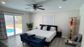 Une chambre avec un lit, un ventilateur de plafond, un bureau, une chaise et une vue sur une piscine.