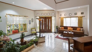 Un salón amplio con un sofá, una mesa de centro y una mesa de comedor. Hay plantas en macetas y una ventana con cortinas.