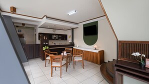 Una cocina moderna con comedor, televisor montado en la pared y una escalera que sube a otro nivel.