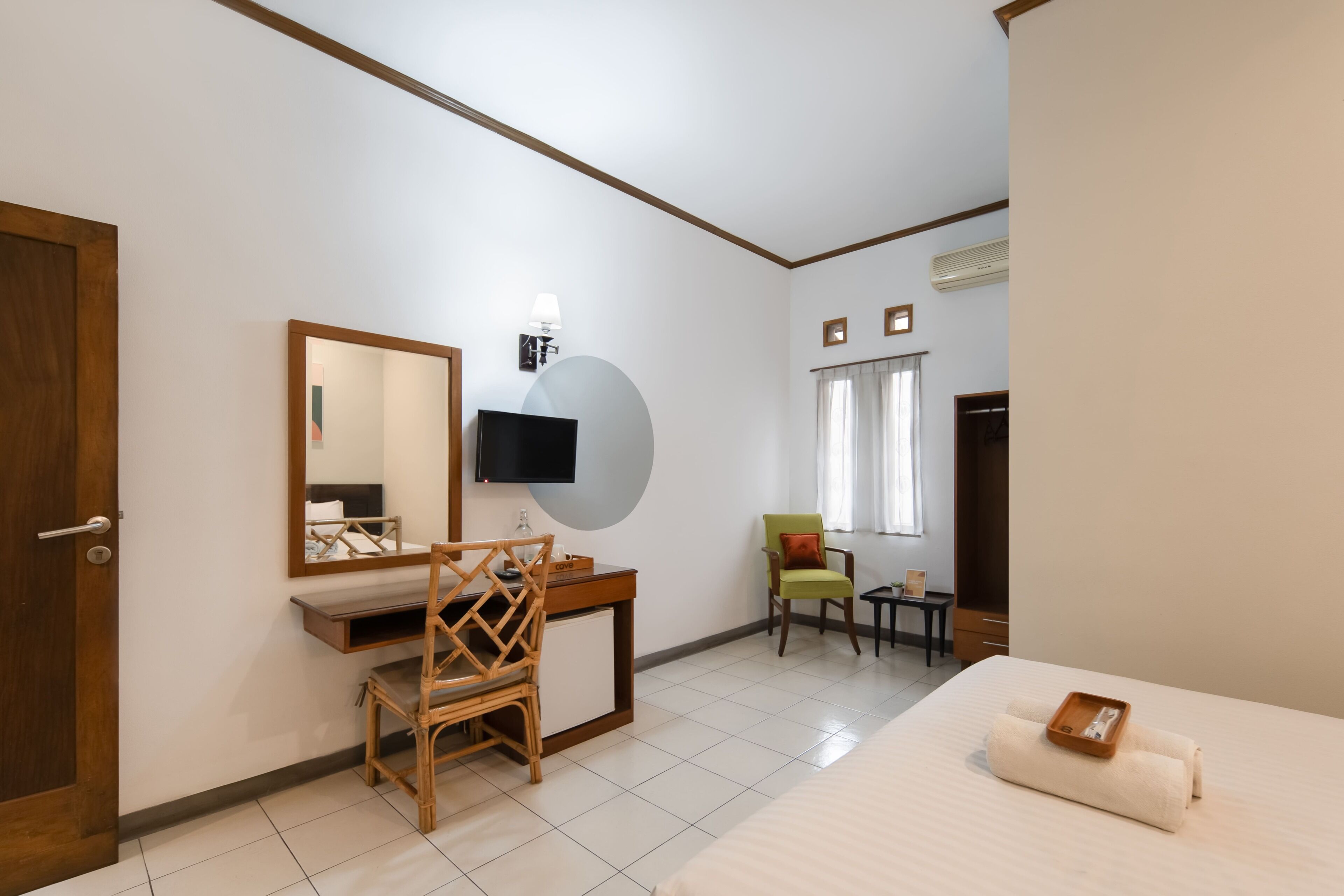 Una camera d'albergo con un letto, una scrivania con una sedia, una televisione, uno specchio e una finestra con tende.