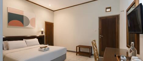 A hotel room with a bed, bedside table, TV, and a small seating area.