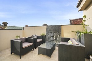 A rooftop patio with wicker furniture, a Buddha statue, and potted plants. - Launceston Townhouse Hospital, CBD & Cafes (Launceston)