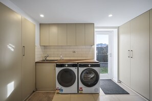 A compact laundry room with two front-loading washing machines, a sink, and a small countertop. - Launceston Townhouse Hospital, CBD & Cafes (Launceston)