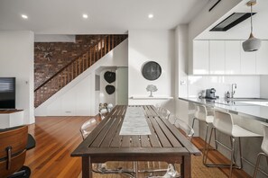 A modern kitchen with white cabinets, a wooden dining table, and a staircase leading to a loft area. - Launceston Townhouse Hospital, CBD & Cafes (Launceston)