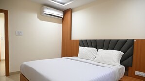 Een net opgemaakt bed met een houten hoofdbord, een nachtkastje en een airconditioner aan de muur.