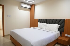 Una cama bien hecha con cabecera de madera, una mesita de noche y un equipo de aire acondicionado montado en la pared.