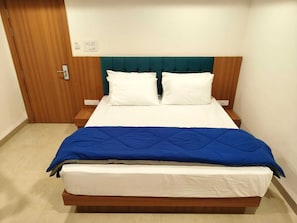 Une chambre Ă coucher avec un cadre de lit en bois, une tĂȘte de lit recouverte dâun tissu turquoise, du linge de lit blanc et une couverture bleue.