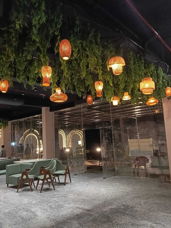 Un restaurante con faroles colgantes, asientos acolchados verdes y un separador de vidrio.