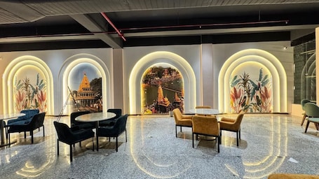 A lobby with a modern design, featuring a central seating area with round tables and chairs, and large arched windows with illuminated frames.. Shubh Ratna Resort