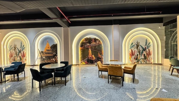A lobby with a modern design, featuring a central seating area with round tables and chairs, and large arched windows with illuminated frames.