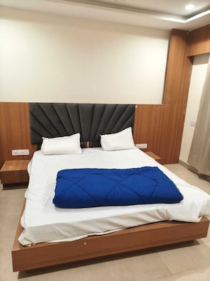 Un lit avec un cadre en bois, des draps blancs et une couverture bleue. Il y a deux tables de chevet avec des lampes.