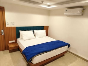 Un dormitorio con una cama, una puerta de madera, aire acondicionado instalado en la pared y una mesita de noche pequeña.