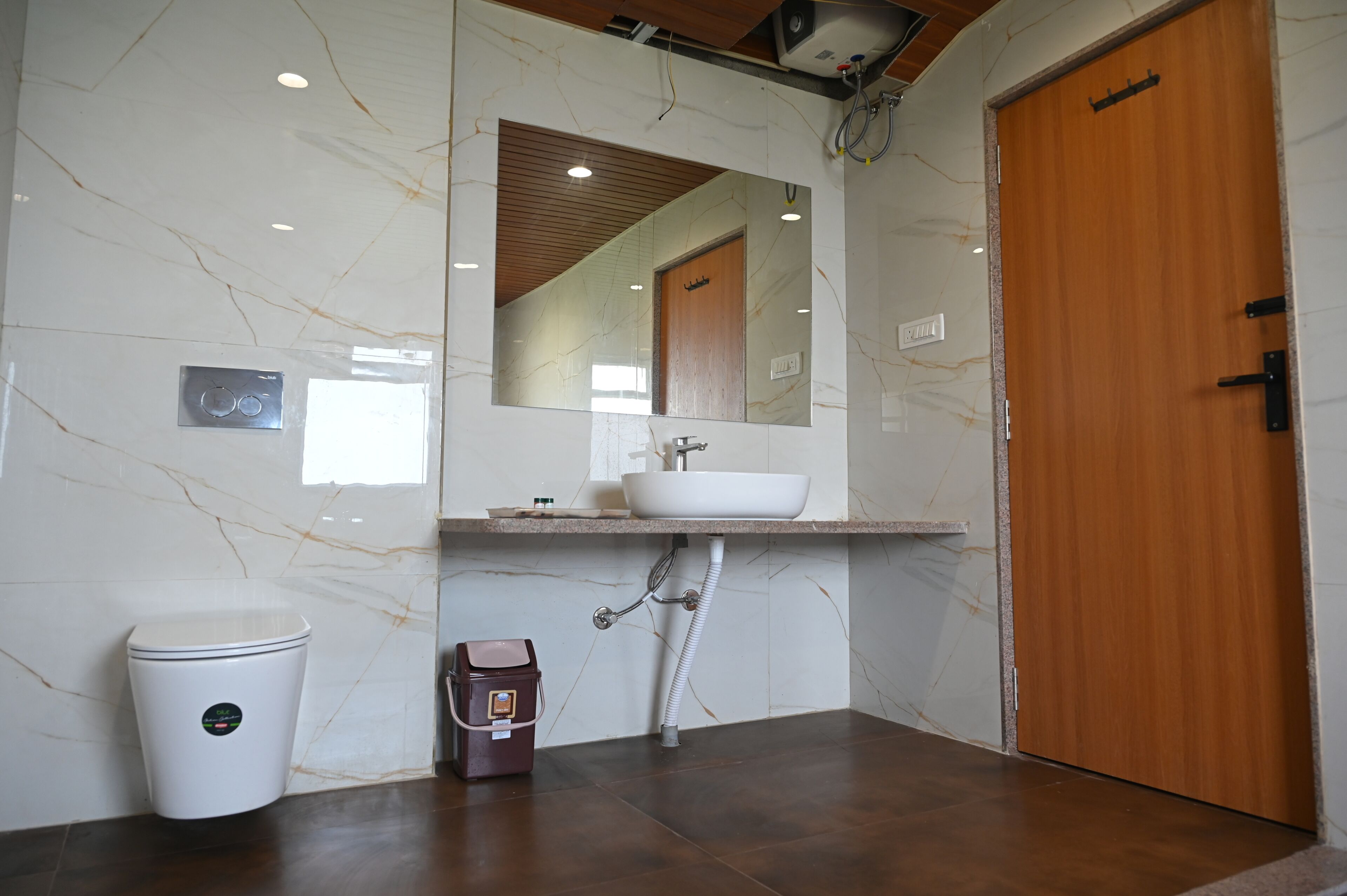 A bathroom with a marble wall, a wooden door, a white sink, and a toilet.