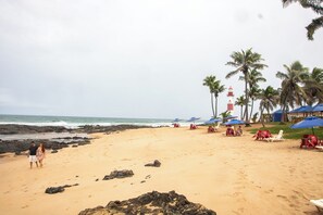 Une plage avec des chaises et des parasols, un phare et des palmiers.