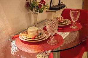 A dining table with a glass top, red placemats, and a vase with flowers. - Ed. Studio Oceânico (Salvador)