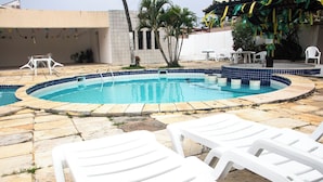 A swimming pool with a tiled edge, surrounded by stone tiles and white lounge chairs. - Ed. Studio Oceânico (Salvador)