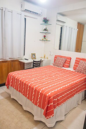 Una camera da letto con un letto, una scrivania, una sedia, uno specchio e una mensola con oggetti decorativi.
