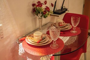 Une table à manger avec un plateau en verre, des sets de table rouges et un vase rempli de fleurs rouges.
