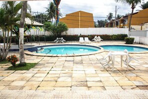 Una piscina con dos sillas de descanso y una mesa, rodeada de baldosas de piedra y palmeras.