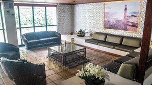 A spacious living area with two sofas, a coffee table, and a large window with a view of the sea. - Ed. Studio Oceânico (Salvador)