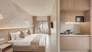 A modern hotel room with a bed, bedside tables, a flat-screen TV, a kitchen area with a microwave, a kettle, and a sink. - Thadatra Inn (Phnom Penh)