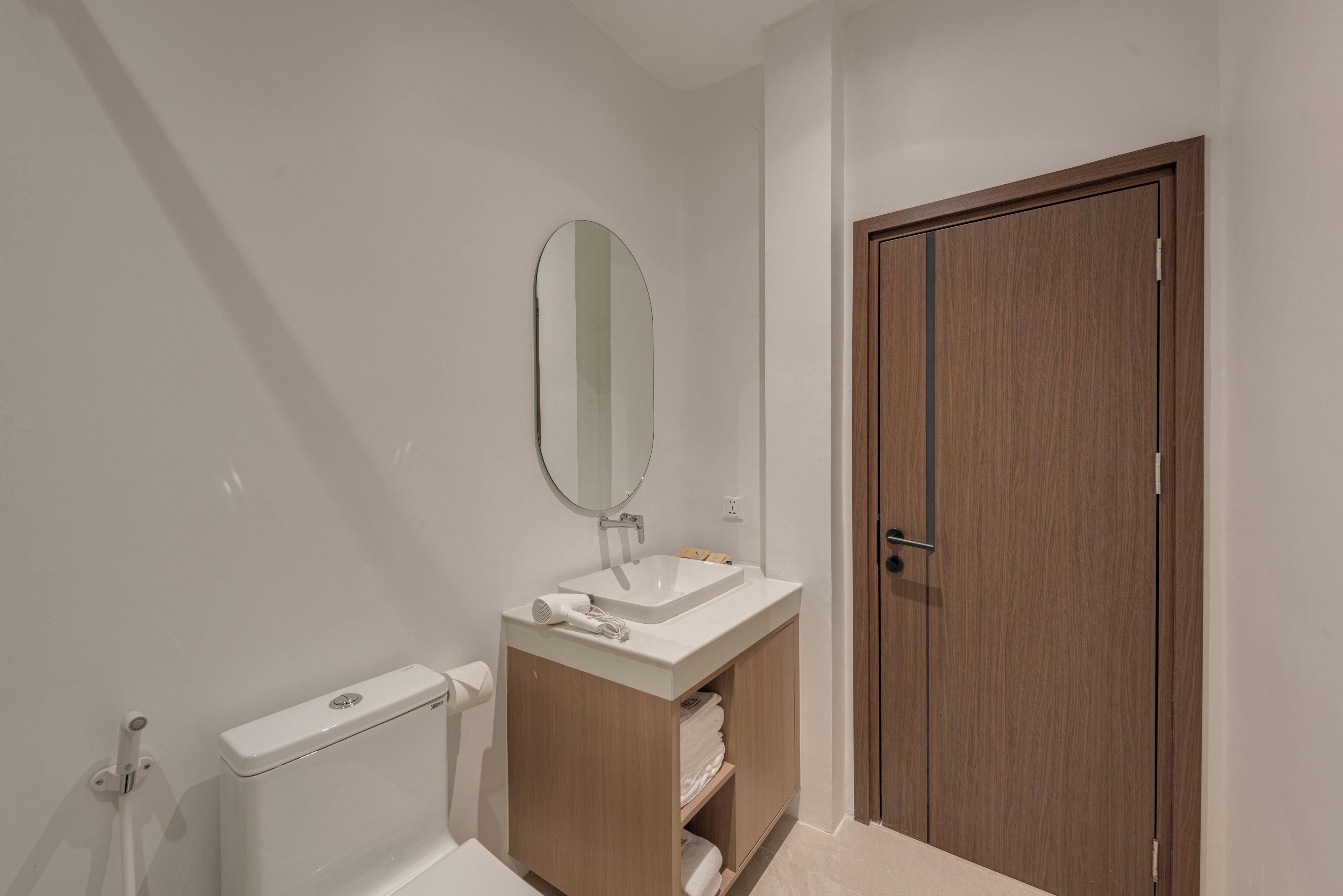 Un baño con un lavamanos blanco, un espejo, un perchero para toallas y una puerta de madera.