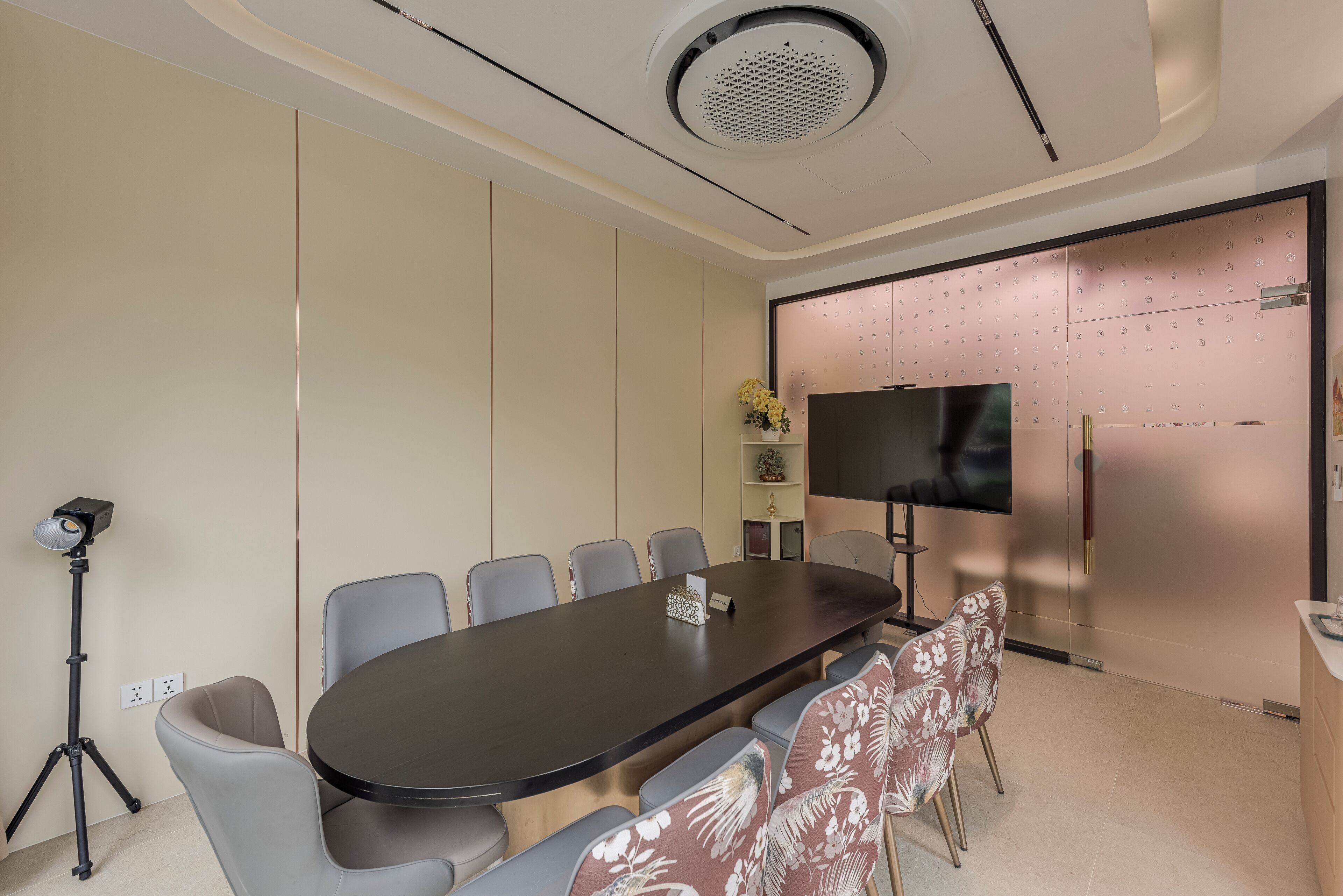 Una sala de conferencias con una larga mesa, sillas, un trípode y un televisor en la pared.