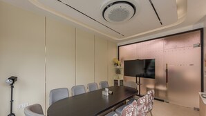 Une salle de conférence avec une longue table, des chaises, un trépied et un téléviseur fixé au mur.