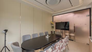 Una sala de conferencias con una larga mesa, sillas, un trípode y un televisor en la pared.