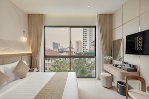 A hotel room with a large bed, a desk, a TV, and a view of the city. - Thadatra Inn (Phnom Penh)