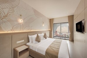 A modern hotel room with a large bed, a bedside table, a flat-screen TV, and a city view through the window. - Thadatra Inn (Phnom Penh)