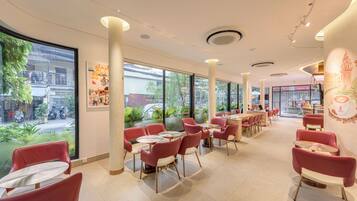 Un interior de cafetería moderno con sillas rojas, mesas redondas, ventanas amplias y vistas a la calle.