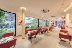 A modern cafe interior with red chairs, round tables, large windows, and a view of the street. - Thadatra Inn (Phnom Penh)