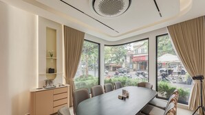 Une salle de conférence dotée d’une grande table ovale, de chaises beiges, d’un petit meuble et offrant une vue sur la rue grâce à de grandes fenêtres.
