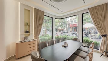 Un salón de conferencias con una gran mesa ovalada, sillas color beige, un mueble bajo y vistas a la calle a través de amplios ventanales.