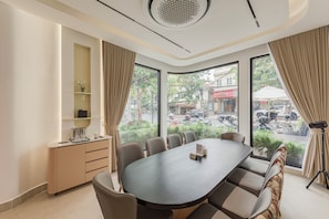 A conference room with a large oval table, beige chairs, a small cabinet, and a view of the street through large windows. - Thadatra Inn (Phnom Penh)