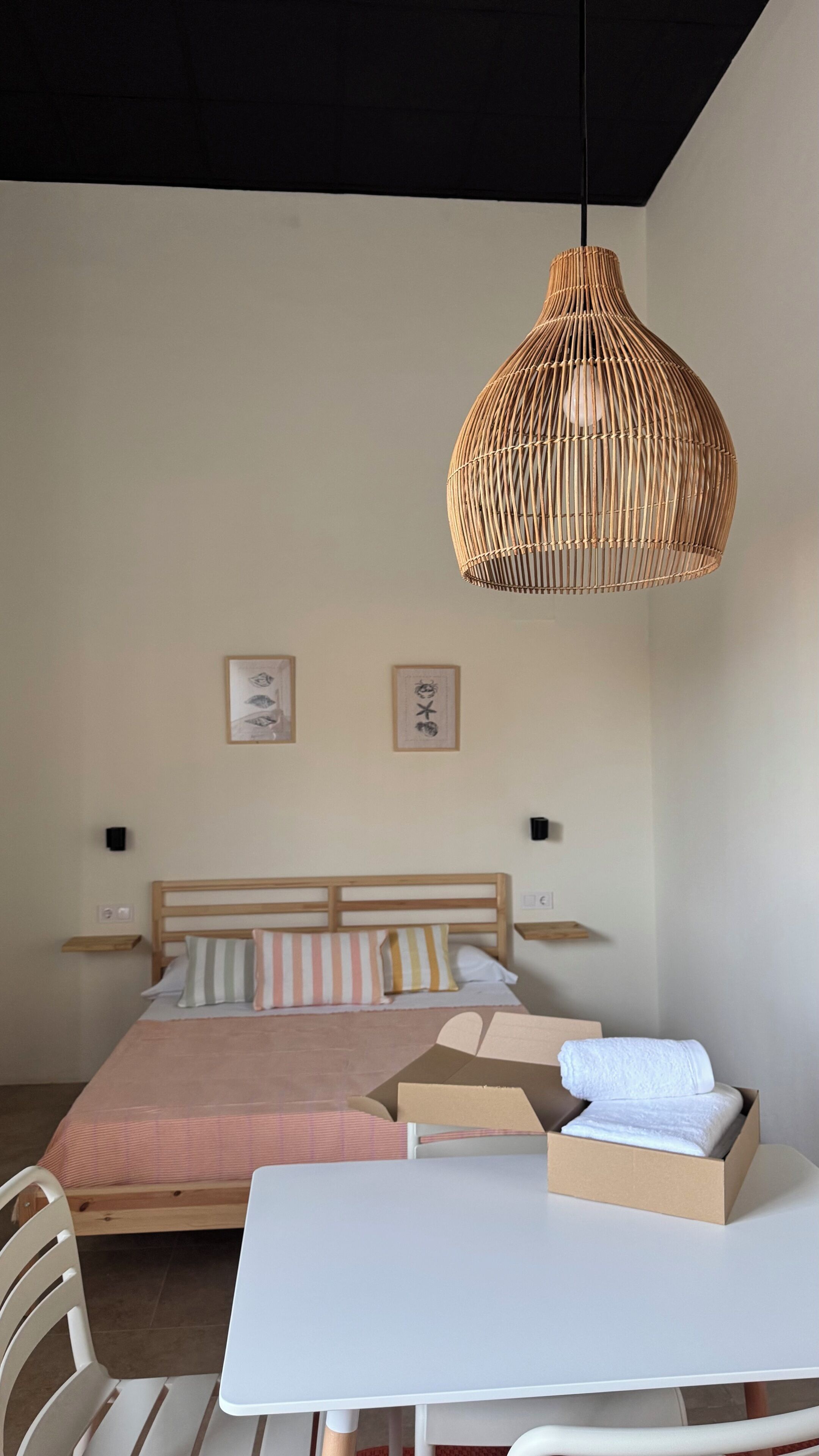 Een slaapkamer met een bed, nachtkastjes, een hanglamp en een tafel met een doos en handdoeken.