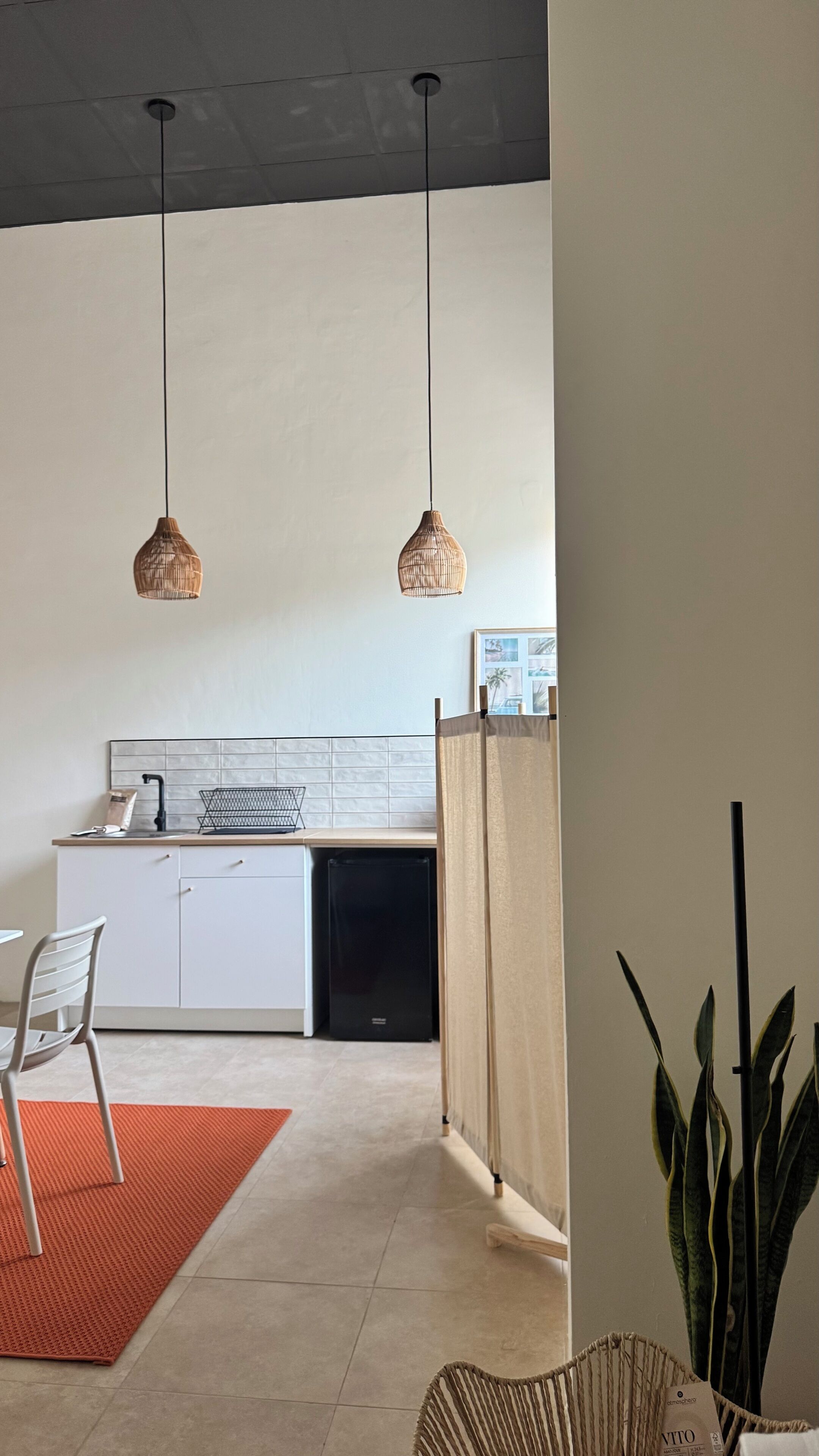 Een moderne keuken met witte kastjes, een zwarte vaatwasser en twee hangende rieten pendellampen.