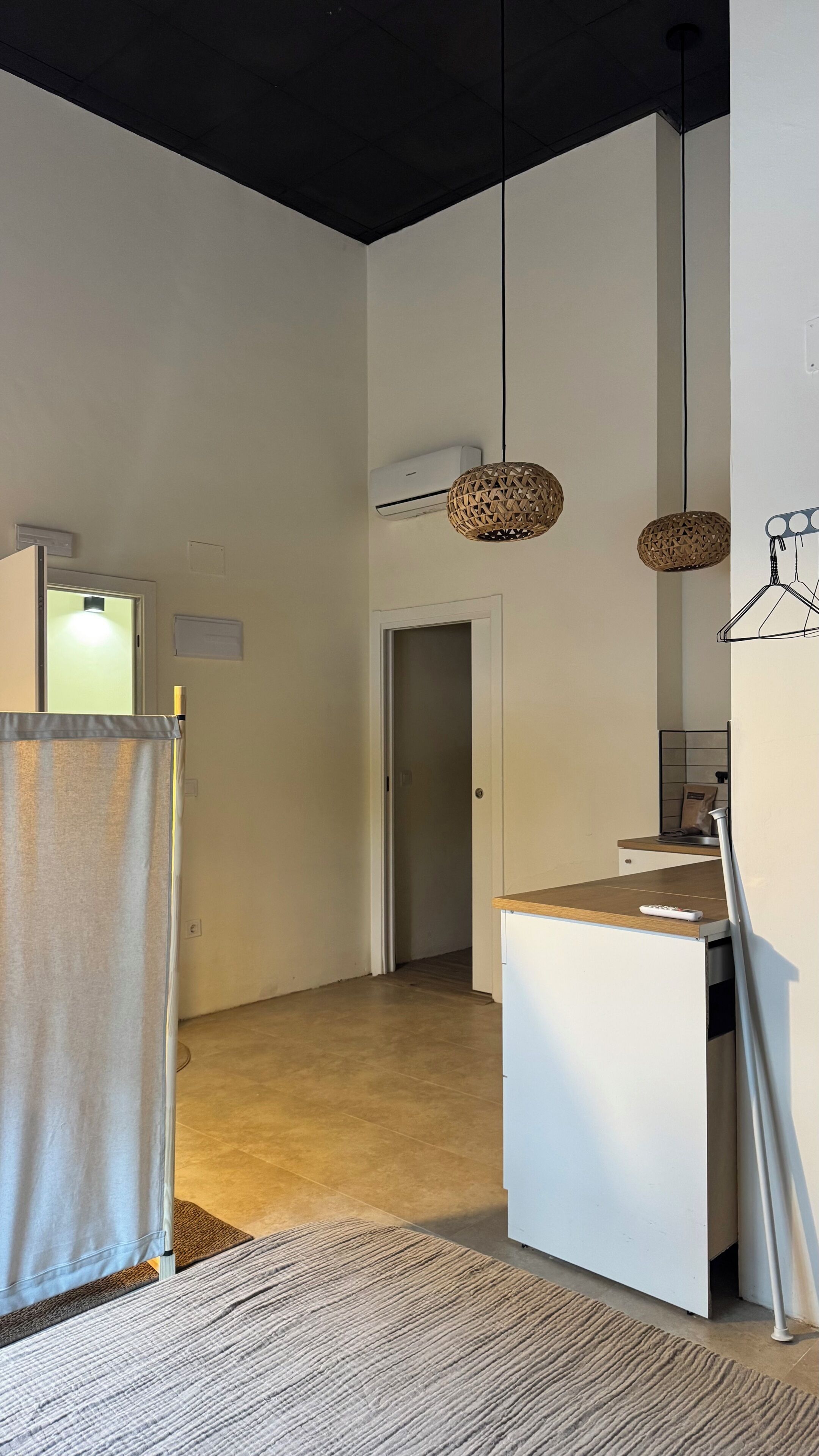 A modern interior with a kitchen area, a doorway leading to another room, and a hanging light fixture.
