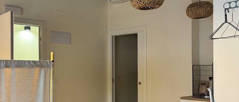 A modern interior with a kitchen area, a doorway leading to another room, and a hanging light fixture.