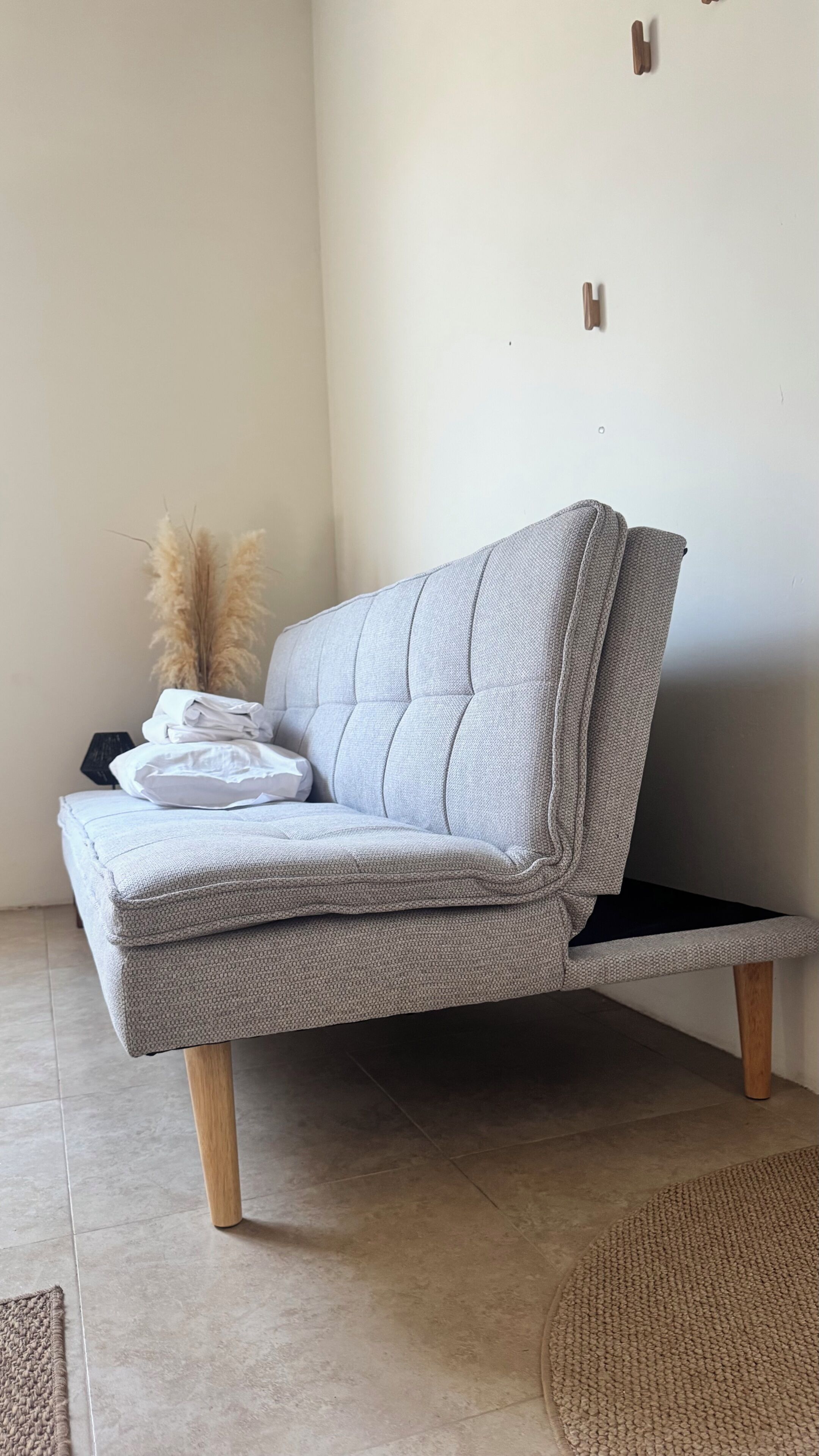 A grey sofa with wooden legs, a folded white pillow, and a decorative plant.