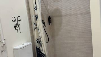 A bathroom with a toilet, shower, and a wall-mounted toilet paper holder.