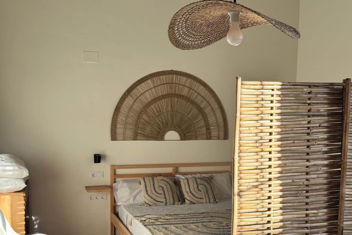 Un dormitorio con cama, una mesa, sillas, una lámpara colgante y un adorno de pared tejido.