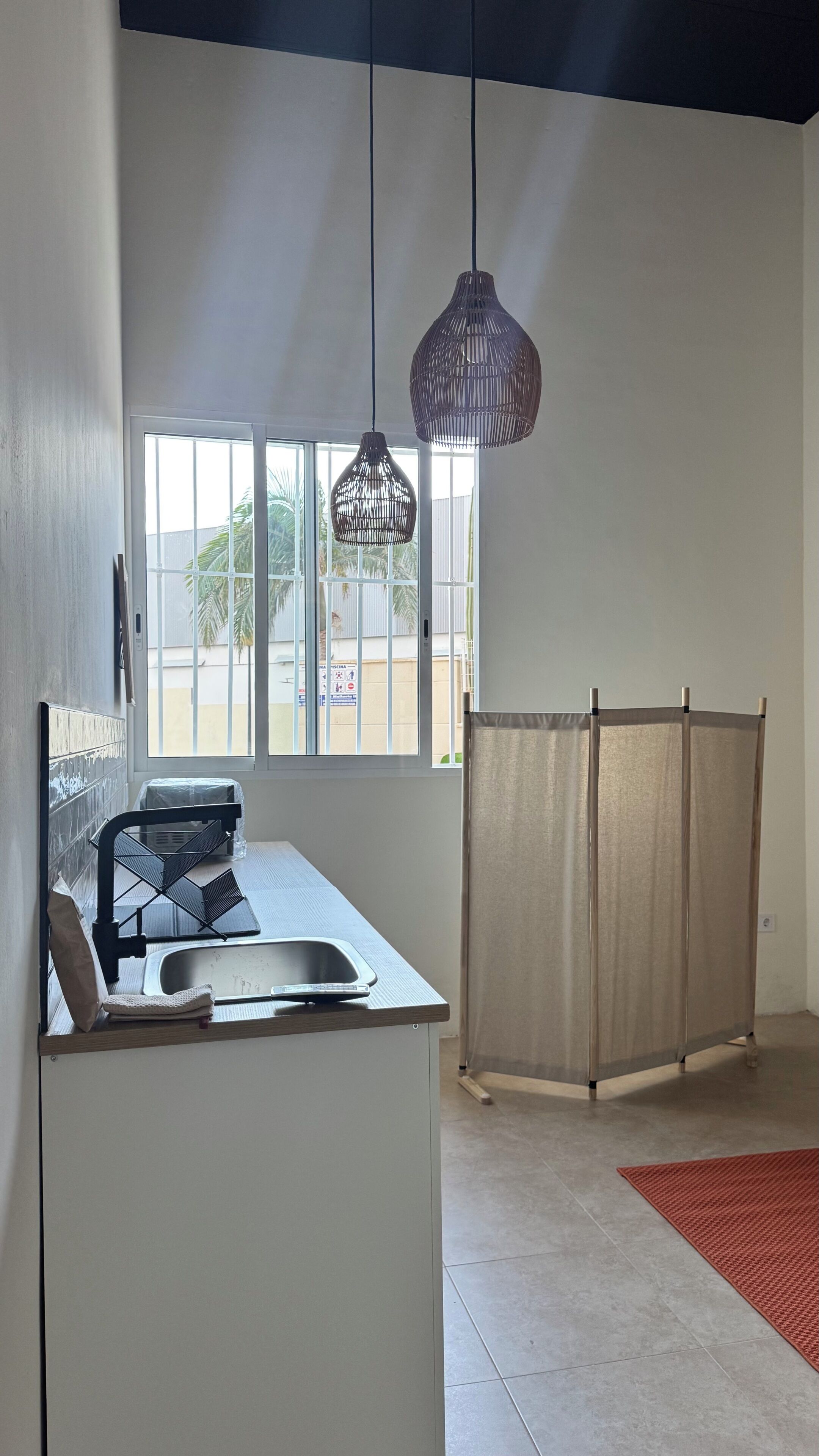 A kitchen with a window, a sink, a chair, and a partition.